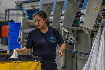 Bow Valley Linen employee Carol feeding flat sheets into one of the Kannegiesser irons